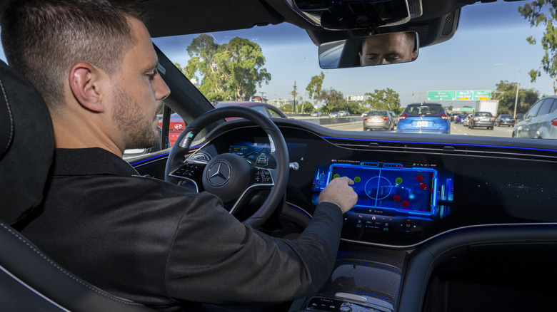 A man behind the wheel of a Mercedes EQS driving on the freeway with Level 3 Drive Pilot active, playing a game on the infotainment screen while the car drives