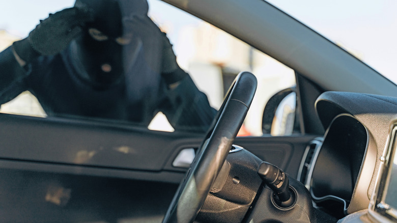 A person in balaclava looking into a car to steal it