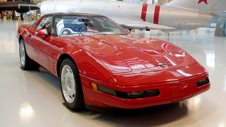 A red 1990 Chevrolet Corvette C4 ZR-1 in front of a fighter plane