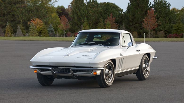A white 1966 Corvette Stingray parked in an open lot with trees in the background.