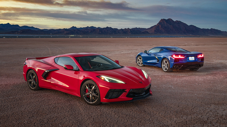 Red and Blue C8 Corvette Stingrays parked on a dry lake bed with mountains in the background.