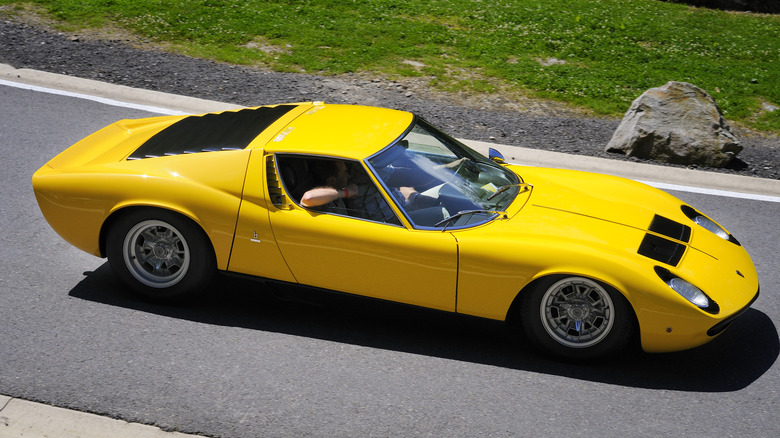 A yellow Lamborghini Miura drives down a road