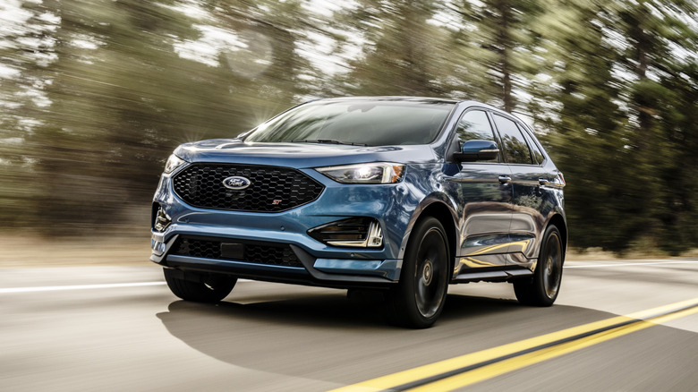 A blue 2019 Ford Edge SUV driving on a road with motion-blurred trees in the background