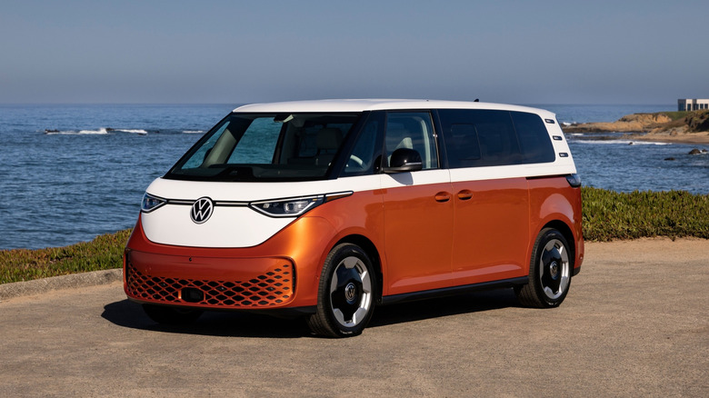 Front 3/4 view of a bronze-white 2025 Volkswagen ID.Buzz parked in front of a seashore