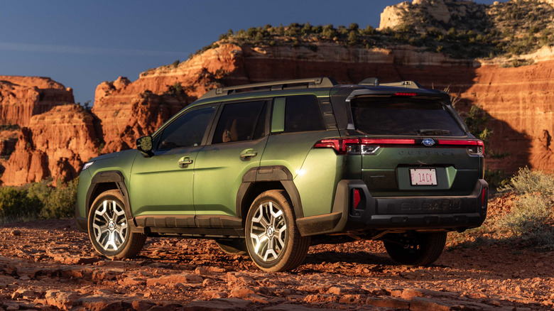 A green Subaru Outback parked in the sunshine in a rocky area.