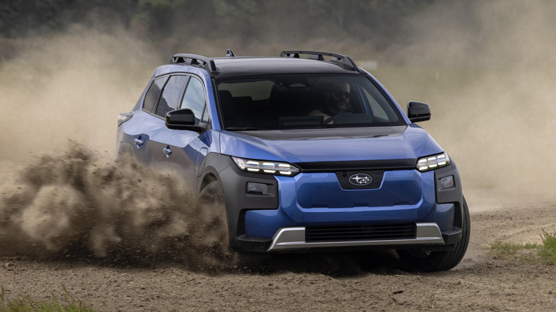 A blue Subaru Trailseeker speeding around a corner on a gravel road, kicking up stones and dust.