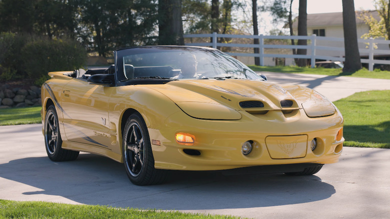 2002 Pontiac Firebird WS6 yellow convertible pulls up to a driveway.