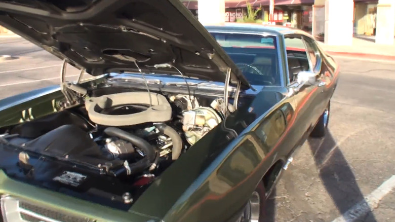 A green 1969 Pontiac GTO sits in a parking lot with its hood popped.