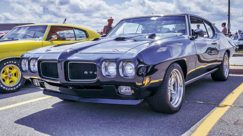 A gleaming black Pontiac GTO sits under the sun at a car show.