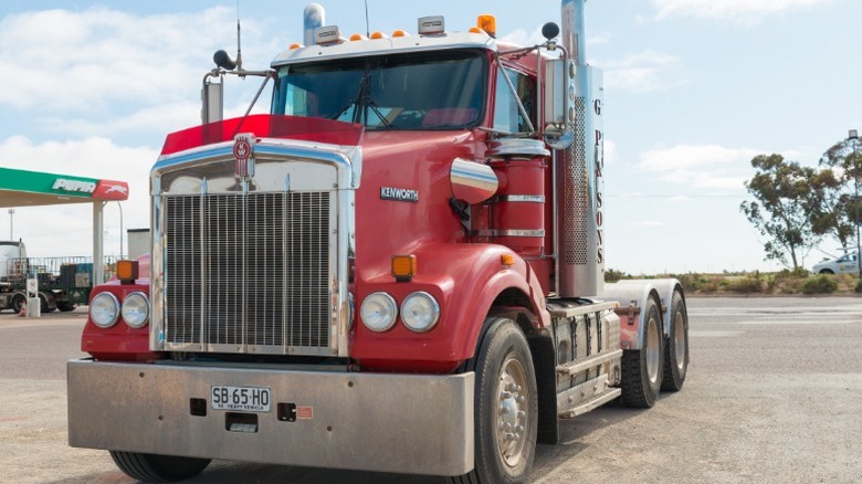 A red Kenworth semi truck parked in front of a gas station