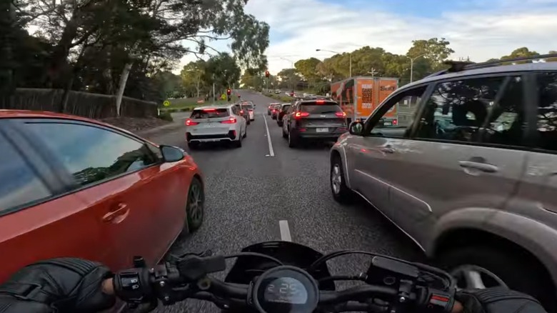Motorcyclist lane-filtering between cars stopped at traffic light