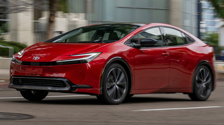 Supersonic red 2026 Toyota Prius XLE driving down city street with buildings in the background