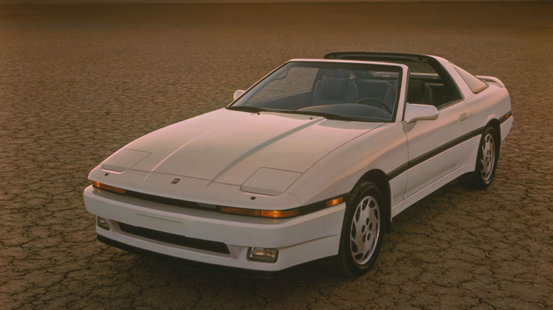 A white Toyota Supra parked on dried-up ground with its roof removed.