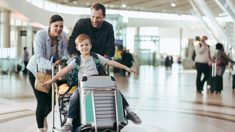 A young boy going for a ride on his parents' luggage in an airport
