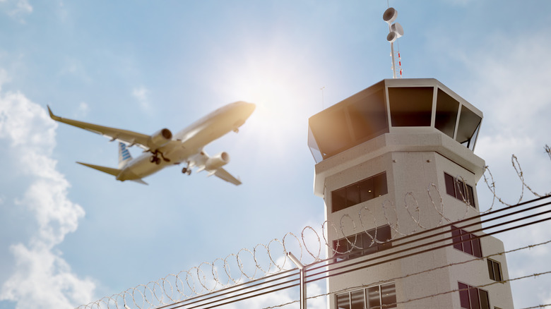 An air traffic control tower underneath the sun as an airliner flies past