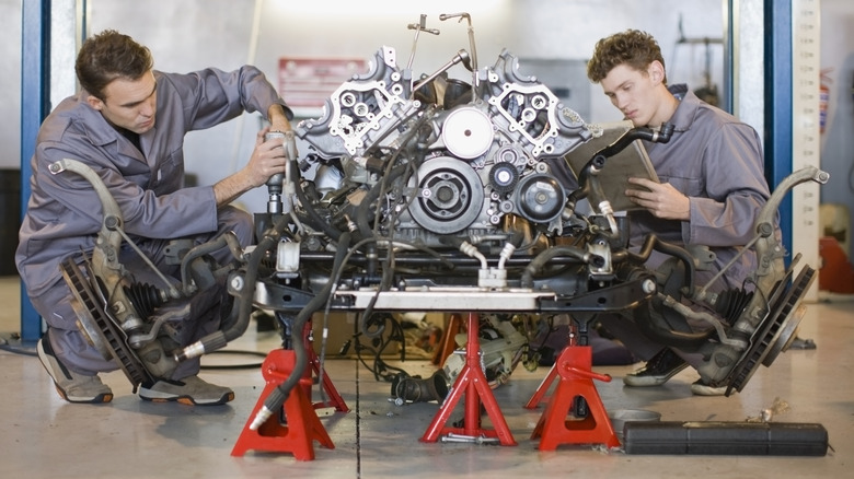 Two technicians disassembling a car engine from the front axle