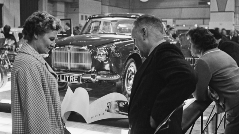 a black and white image of a couple looking at a brochure on the floor of an auto show