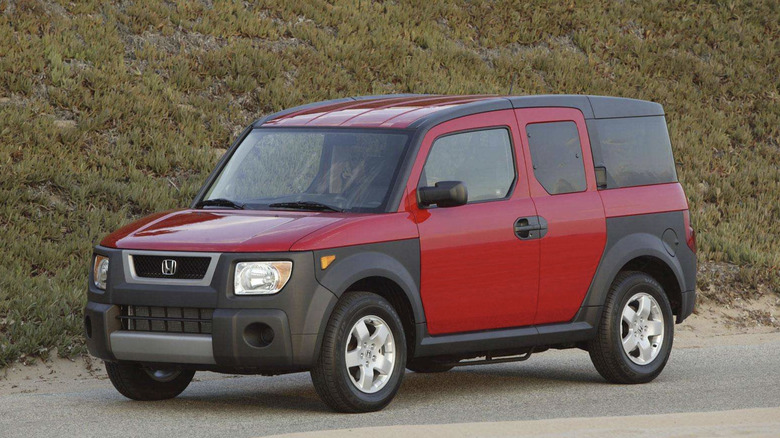 a red honda element parked in front of a grassy hill