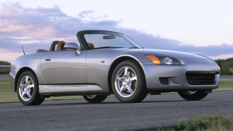 A Honda s2000 parked on a pave stretch of road during a sunset