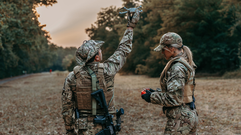 One soldier holds a drone aloft while another holds a controller for it