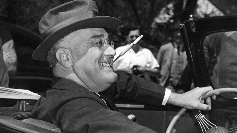 FDR smiling with cigarette in in a holder in his teeth while driving
