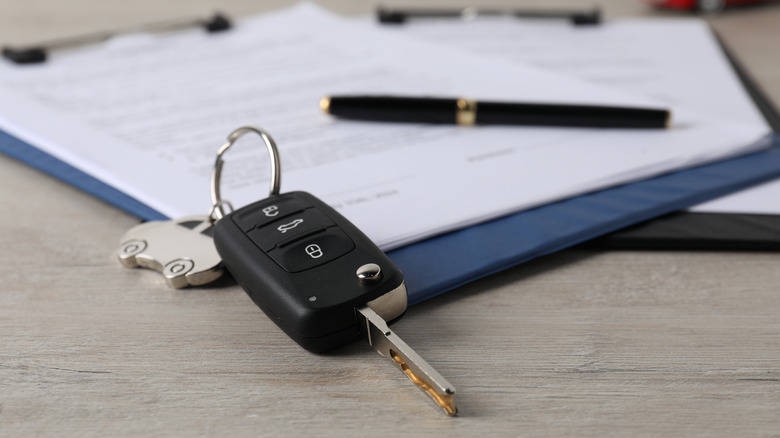 A car keyfob and pen resting on the paperwork to buy a new car.