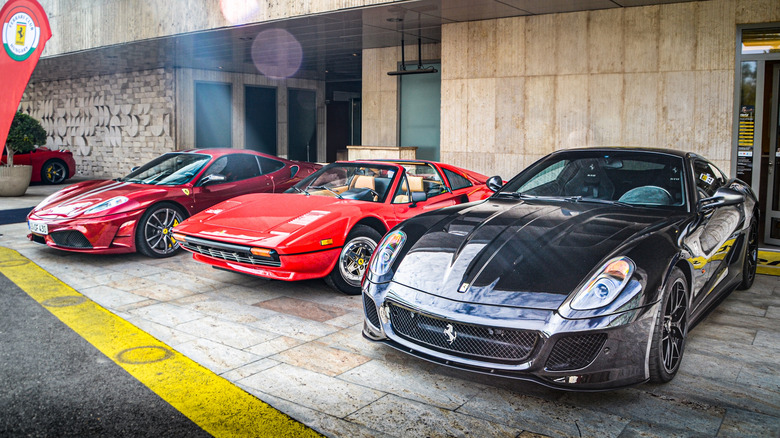 A red Ferrari 430 Scuderia, a red 328 GTS, and a black 599 GTO parked in front of a building