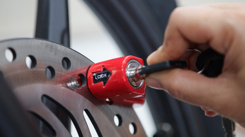 A hand inserts a key into a motorcycle disc-brake lock