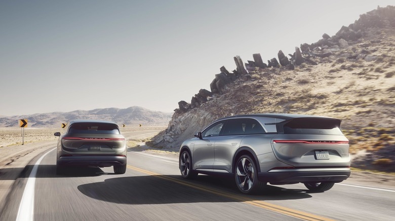 Two Lucid Gravity SUVs drive down a highway rear 3/4
