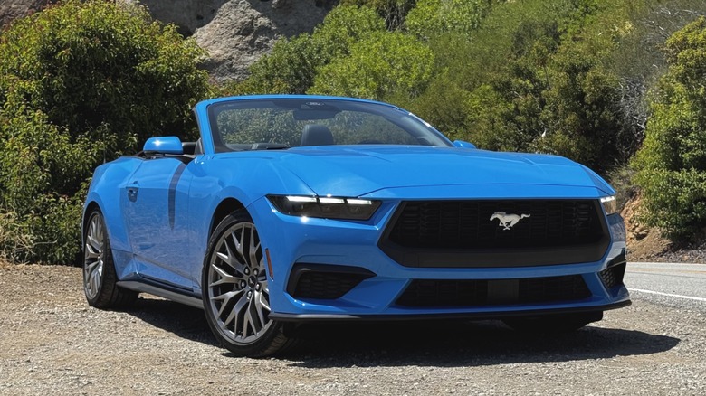front three-quarters shot of a bright blue Mustang Ecoboost convertible parked on dirt with the top down in front of a mountainside
