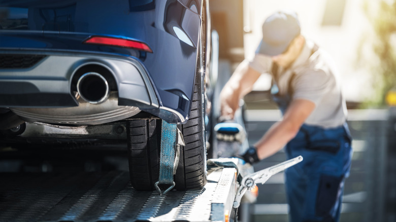 A man secures a blue car to a flatbed tow truck.