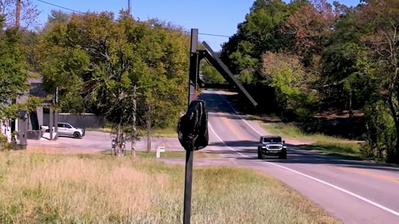 A Flock camera on a pole by a road covered up by a trash bag