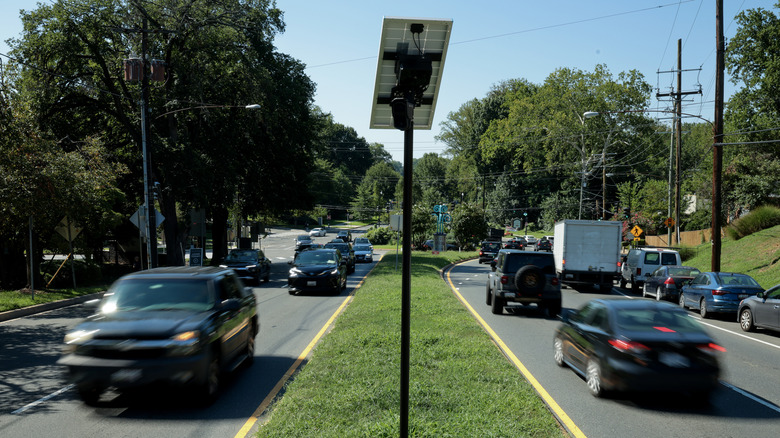An Axon ALPR camera and solar panel mounted on a pole in the median of a busy four-lane road