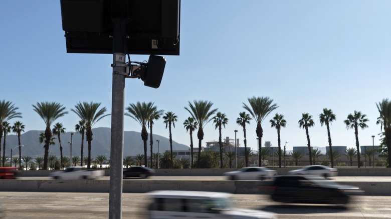 A flock camera positioned over a freeway in California. Palm trees are in the background.