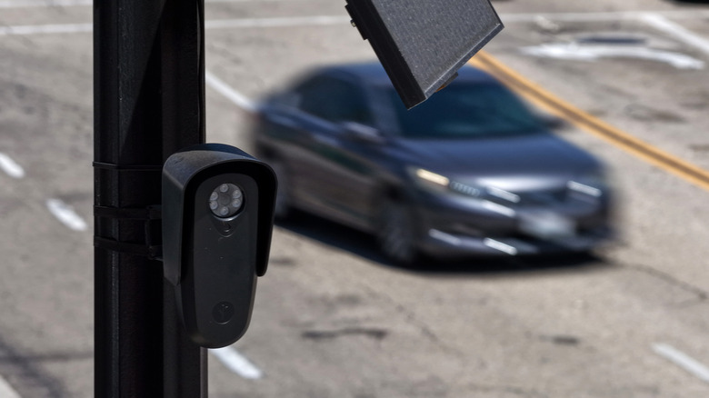 A Flock camera on a pole above a road as a car passes by