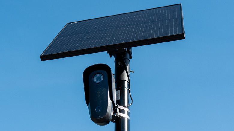 A Flock camera and solar panel on top of a pole against a clear blue sky