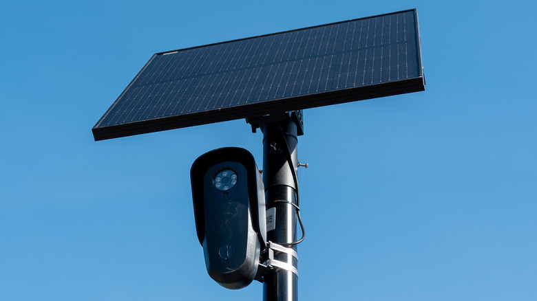 A Flock camera and solar panel mounted on a pole against a clear blue sky