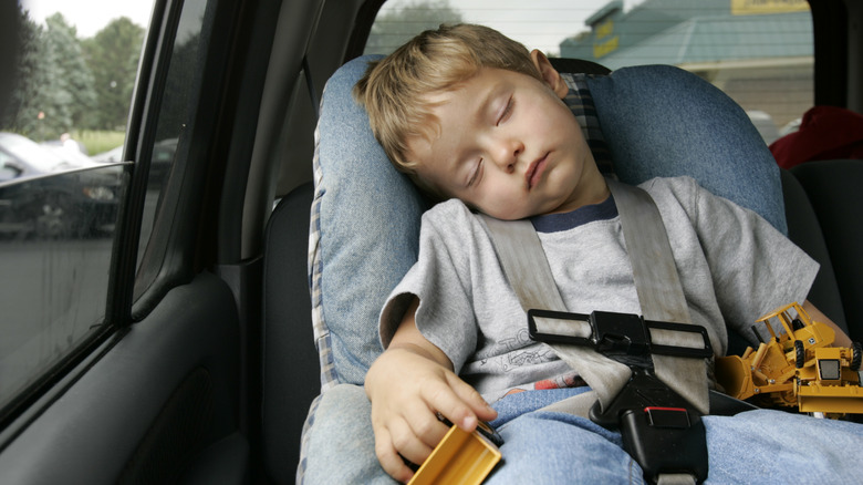 A young boy holding construction toys sleeping in a forward-facing child car seat