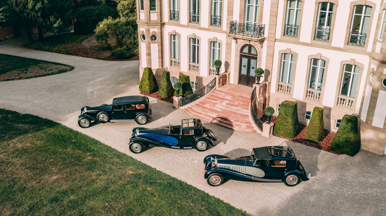 An overhead shot of three Bugatti Type 41 Royale models in front of a fancy house