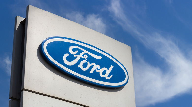 Close-up Ford brand logo on against blue sky background. Dealership centre of car shop