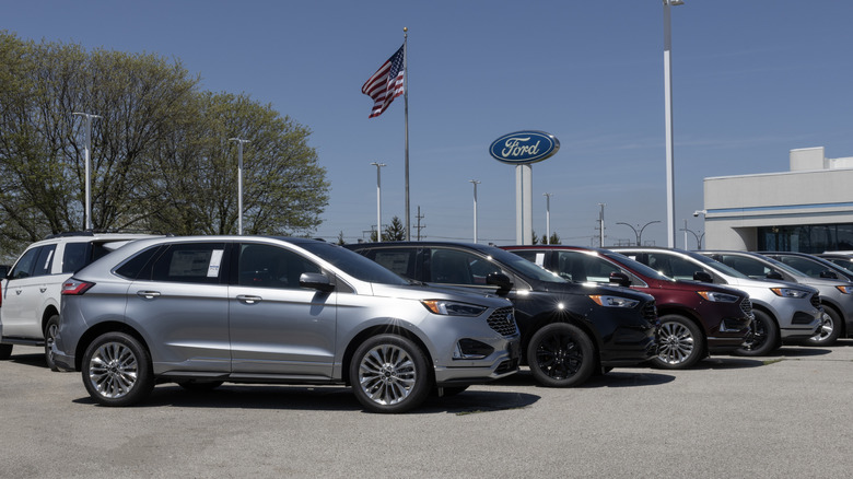 A line of gray, black, red Ford Edge SUVs at a Ford dealership with American flag in background