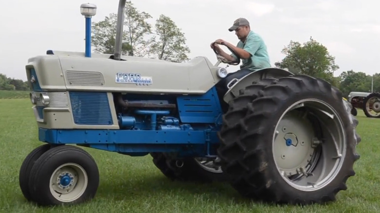 A Ford 6000 diesel tractor with dual rear wheels and a man in a green shirt and blue jeans driving