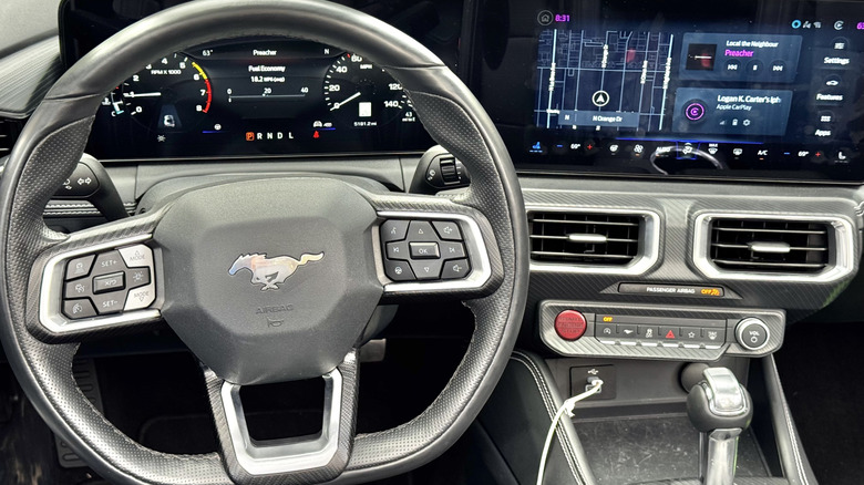 A close-up of the driver's POV in the black interior of the Mustang with the navigation up on the screen