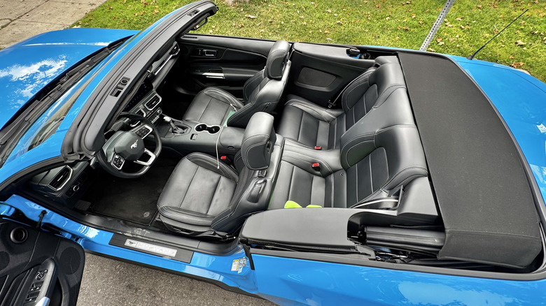 An overhead look down at the interior of the blue Mustang with the top down showing all four of the black leather seats and some green grass on the other side of the car