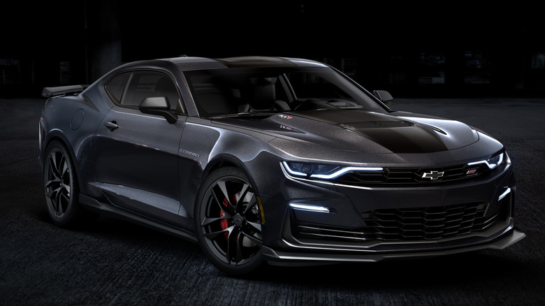 Dark Chevy Camaro parked with its parking lights on.