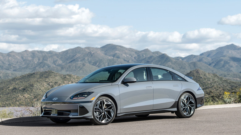 A front three-quarters shot of a gray Hyundai Ioniq 6 parked on asphalt in front of a vista of a mountain range and a blue cloudy sky