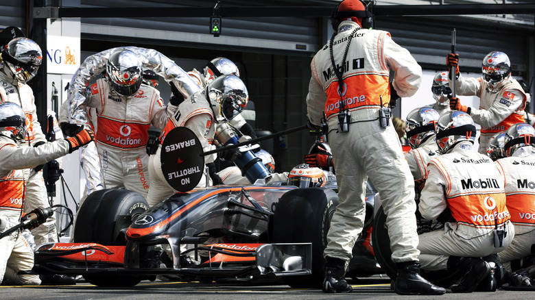 McLaren Formula One racing team mechanics perform a Formula One refuelling and new tyre pit stop on the chrome silver MP4-24 racing car driven by Finnish racing driver Heikki Kovalainen in the pit lane while wearing safety helmets, reflective goggles and visors and logo adorned fire protection suits during the 2009 Belgian Grand Prix, Spa-Francorchamps, Belgium, on the 30th August 2009.