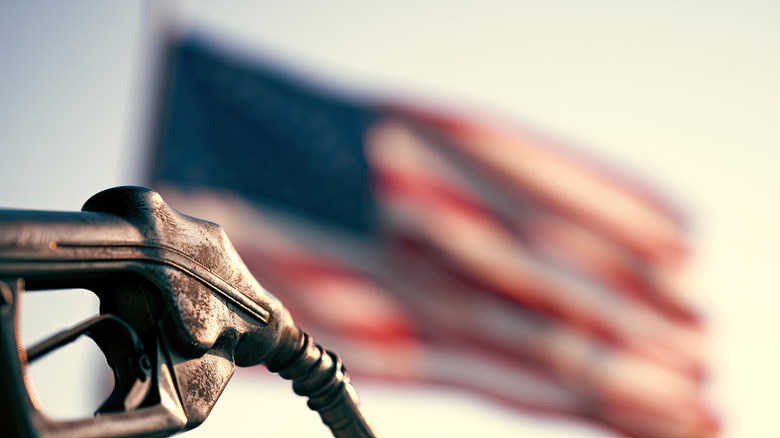 A gas pump in the bottom left frame in focus with the American flag waving, blurred, in the background.
