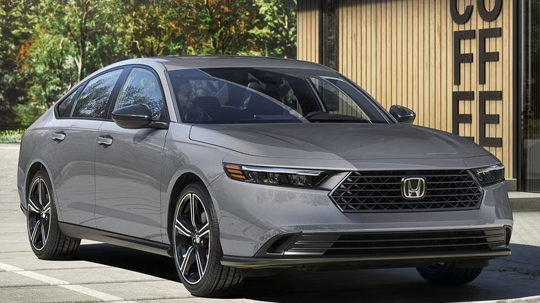 A grey 2026 Honda Accord midsize sedan is parked in a concrete lot next to a coffee shop.