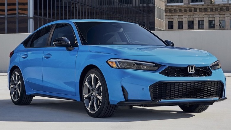 A bright blue 2026 Honda Civic Hatchback Sport Touring Hybrid parked on an open-air concrete rooftop parking deck.
